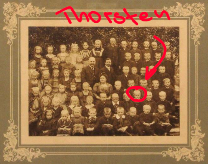 Symbolbild: Schwarzweiß-Foto einer Schulklasse aus dem frühen 20. Jahrhundert mit einem rot markierten Pfeil, der einen jungen in der zweiten Reihe scherzhaft als „Thorsten“ bezeichnet.