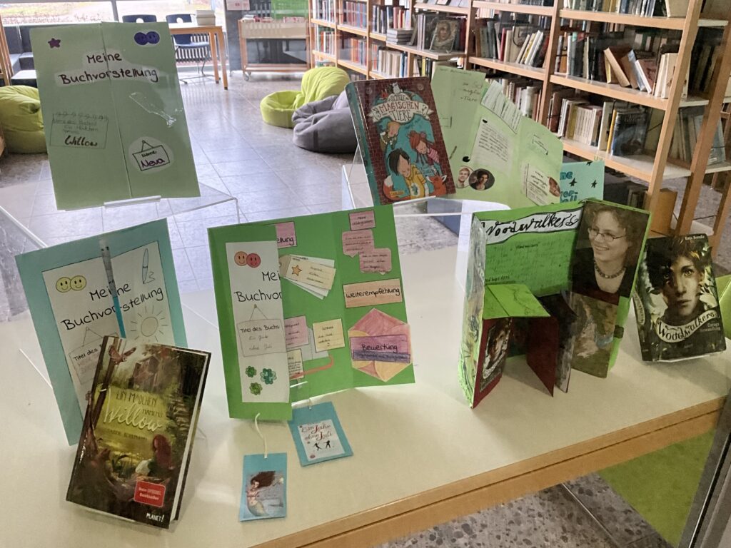 Ausstellungstisch in der Schülerbibliothek. Darauf bunt gestaltete Buchvorstellungen in Flyer- oder Mappenform.