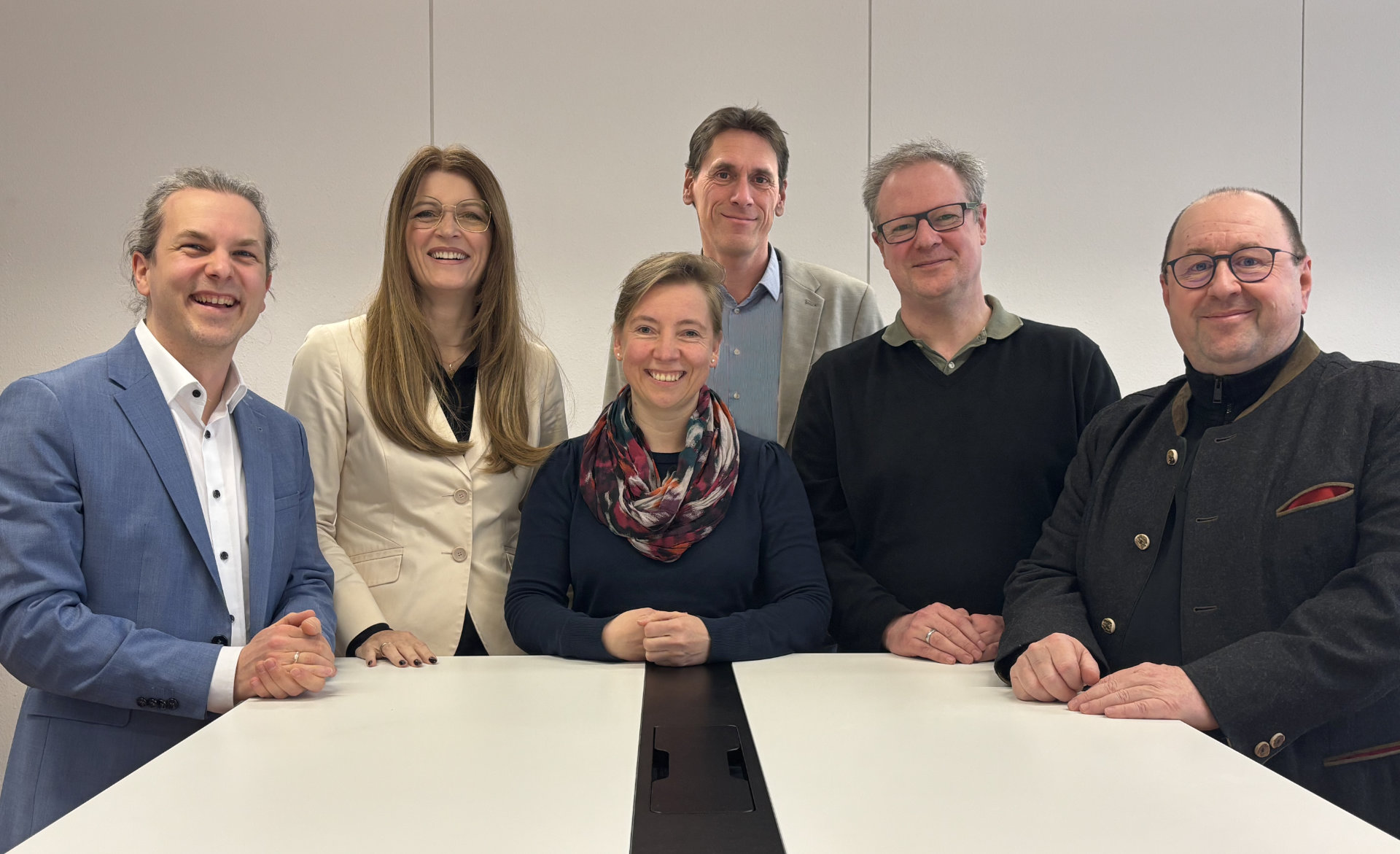 Foto des Schulleitungsteams des HGK. Sechs Personen stehen hinter einem Bürotisch vor einer weißen Wand und lächeln in die Kamera: Hans Bäckel, Christiane Lindörfer-Oberle, Susanne Lederer, Ulrich Hecking, Christian Baum, Wolfgang Heil